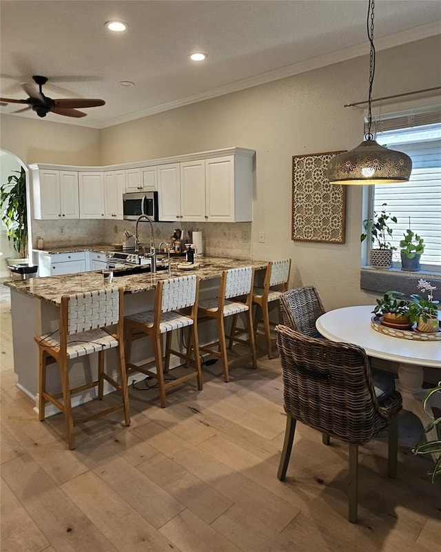 kitchen featuring stainless steel appliances, decorative backsplash, white cabinetry, crown molding, and a kitchen breakfast bar