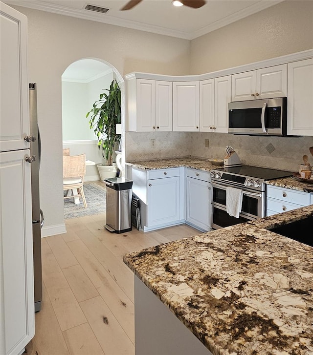 kitchen with ornamental molding, light stone countertops, arched walkways, and stainless steel appliances