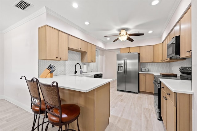 kitchen featuring a breakfast bar, appliances with stainless steel finishes, a peninsula, a ceiling fan, and a sink