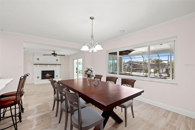 dining area with crown molding, a brick fireplace, baseboards, and light wood finished floors