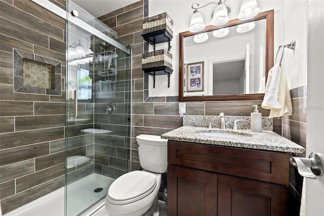 bathroom with toilet, tile walls, a stall shower, and vanity