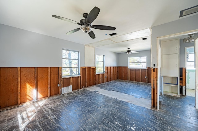 spare room with visible vents, ceiling fan, wainscoting, and wood walls