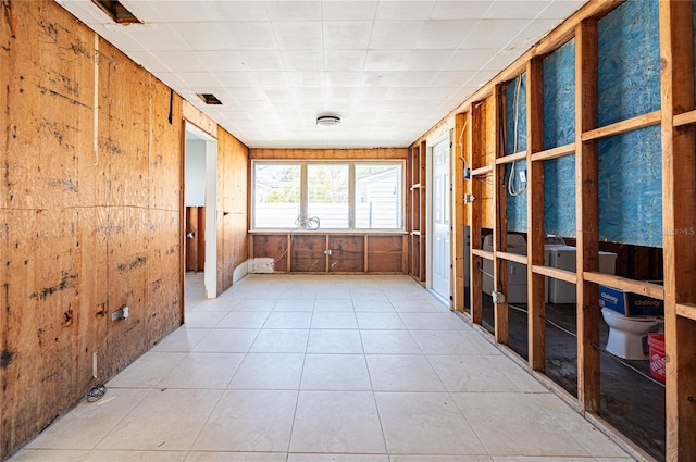 interior space with light tile patterned floors, visible vents, and wood walls