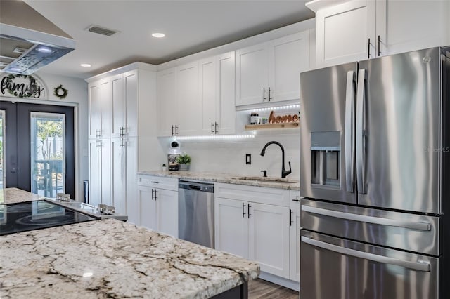 kitchen featuring a sink, stainless steel appliances, white cabinetry, wall chimney exhaust hood, and backsplash