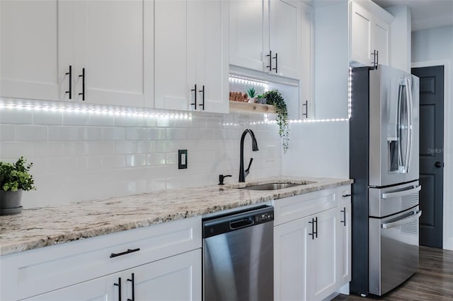 kitchen featuring backsplash, light stone counters, appliances with stainless steel finishes, white cabinetry, and a sink