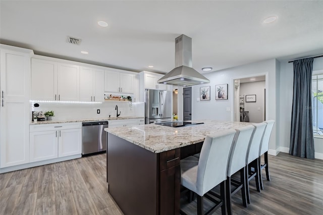 kitchen featuring visible vents, a center island, a kitchen bar, appliances with stainless steel finishes, and island range hood