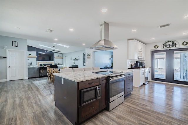 kitchen featuring visible vents, white cabinetry, vaulted ceiling with skylight, appliances with stainless steel finishes, and island range hood