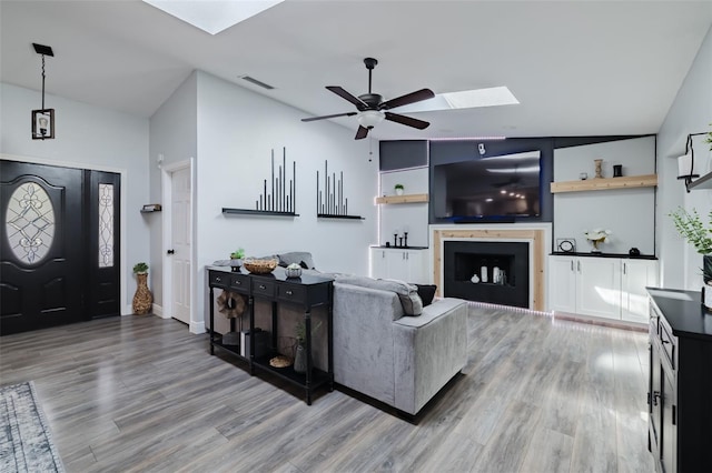 living room with vaulted ceiling with skylight, wood finished floors, visible vents, and ceiling fan