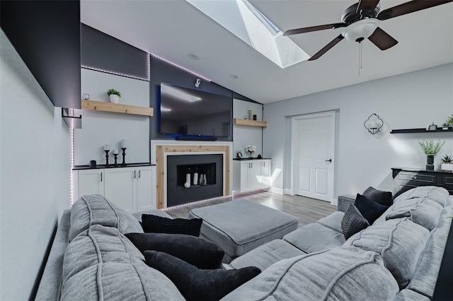 living room with lofted ceiling with skylight, wood finished floors, a fireplace, baseboards, and ceiling fan