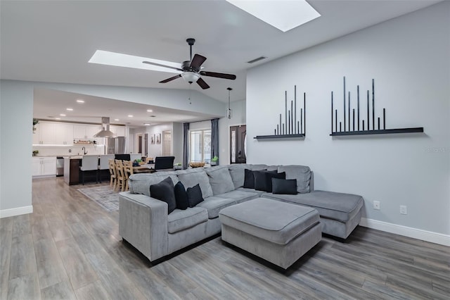 living area with lofted ceiling with skylight, light wood-style flooring, visible vents, and ceiling fan