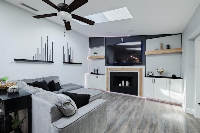 living area with visible vents, ceiling fan, lofted ceiling with skylight, a fireplace, and wood finished floors