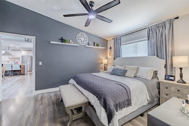 bedroom featuring ceiling fan, baseboards, wood finished floors, and stainless steel refrigerator with ice dispenser