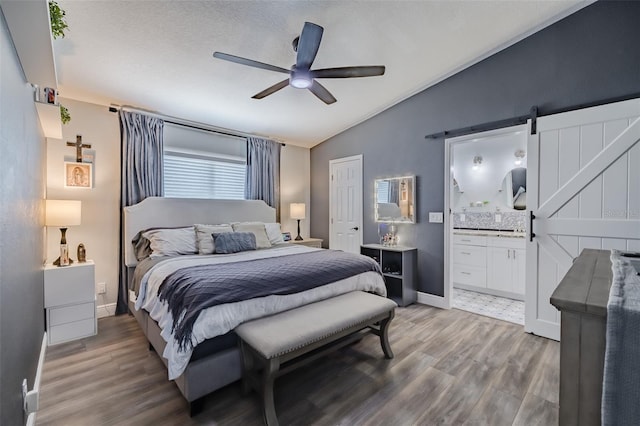 bedroom featuring vaulted ceiling, light wood-style flooring, a barn door, and connected bathroom