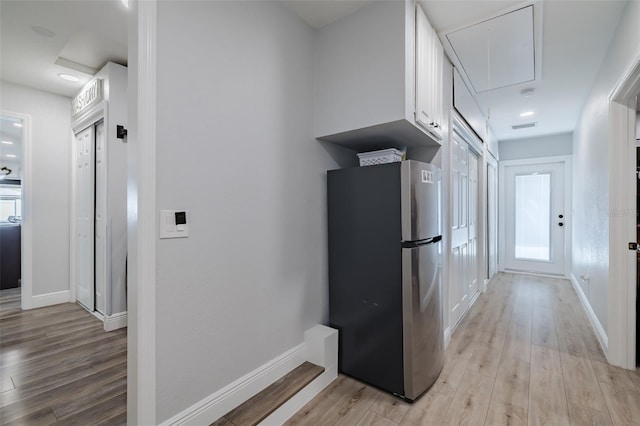 hallway featuring attic access, light wood-style flooring, and baseboards