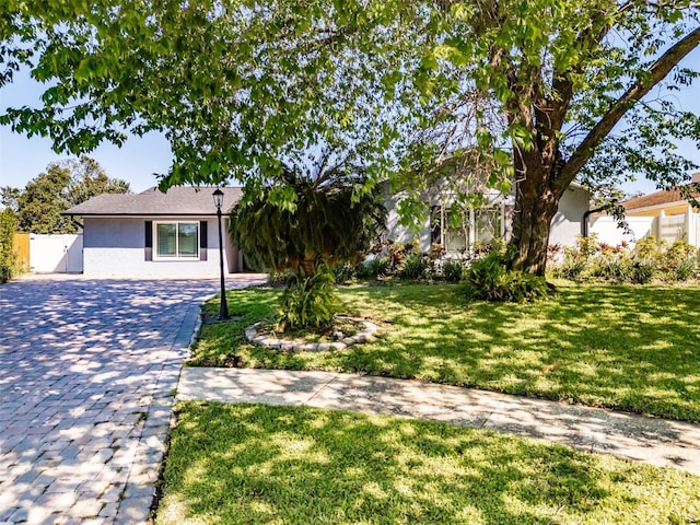 ranch-style home with a front lawn, decorative driveway, fence, and stucco siding