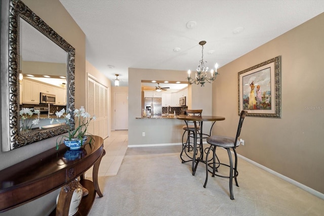 dining space with ceiling fan with notable chandelier, baseboards, and light carpet