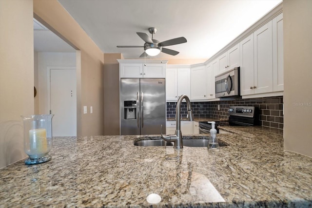 kitchen with a sink, light stone counters, backsplash, appliances with stainless steel finishes, and ceiling fan