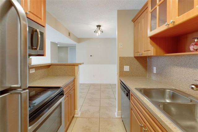 kitchen with glass insert cabinets, light countertops, light tile patterned floors, stainless steel appliances, and a sink