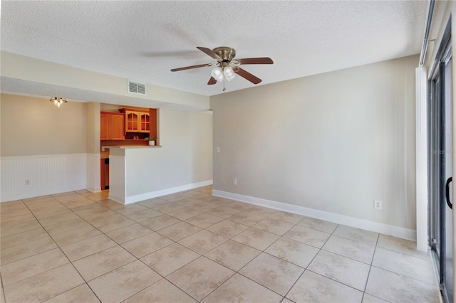 spare room featuring visible vents, light tile patterned floors, wainscoting, a textured ceiling, and a ceiling fan