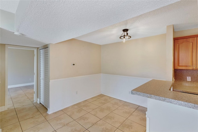 empty room with a textured ceiling, light tile patterned flooring, and wainscoting