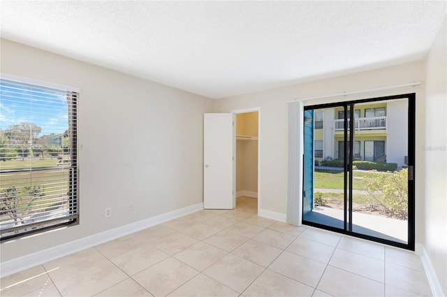 unfurnished bedroom featuring access to exterior, light tile patterned floors, a textured ceiling, and baseboards