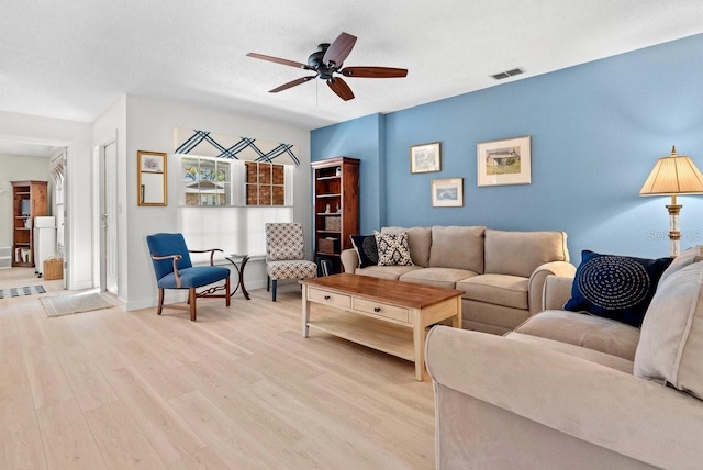 living room featuring visible vents, baseboards, light wood-type flooring, a textured ceiling, and a ceiling fan