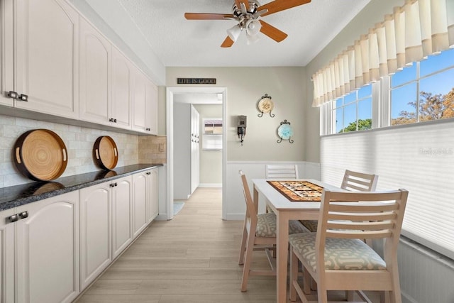 dining room featuring light wood-style flooring, a textured ceiling, wainscoting, and a ceiling fan