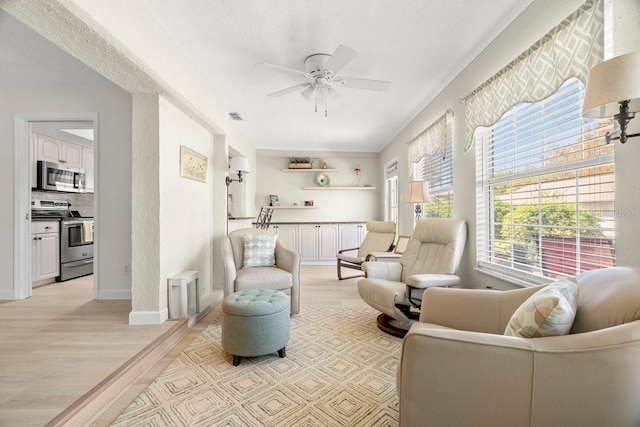 living area featuring a textured ceiling, light wood-style floors, baseboards, and ceiling fan