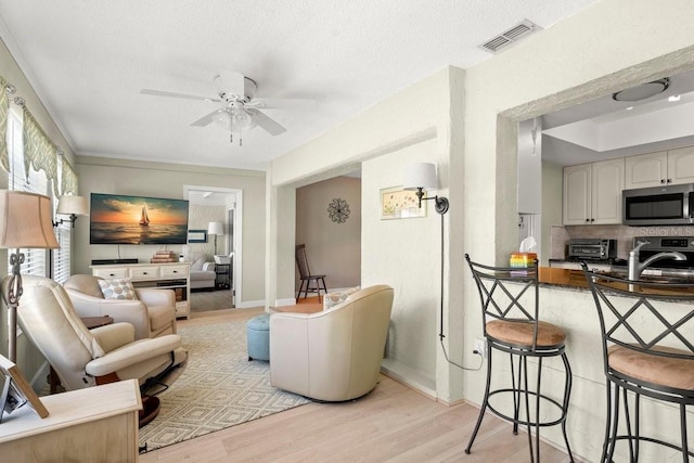 living area featuring visible vents, ceiling fan, a toaster, light wood-type flooring, and a textured ceiling