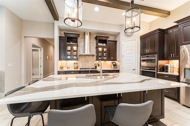 kitchen with beamed ceiling, stainless steel appliances, wall chimney range hood, and a sink