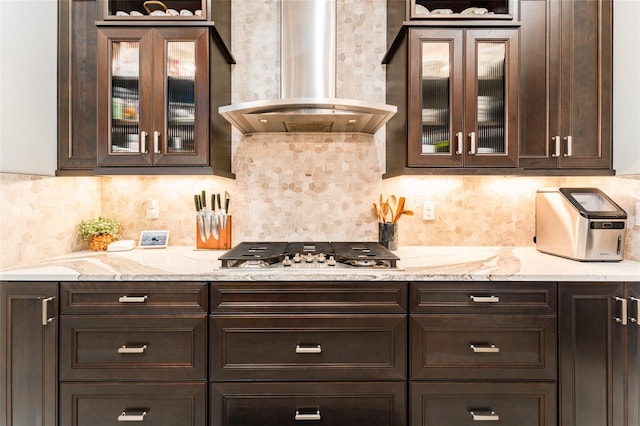 kitchen with dark brown cabinetry, stainless steel gas cooktop, wall chimney exhaust hood, and light stone counters