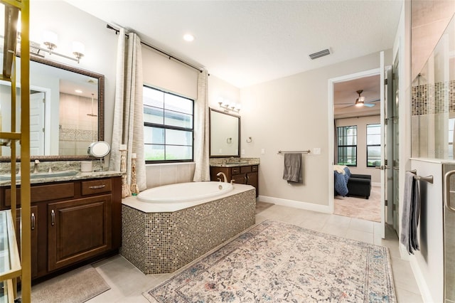 ensuite bathroom featuring tile patterned flooring, visible vents, ceiling fan, two vanities, and a bath