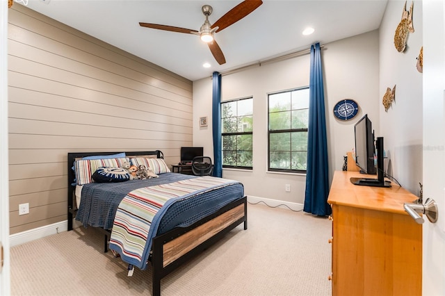 bedroom featuring wooden walls, a ceiling fan, baseboards, and light carpet