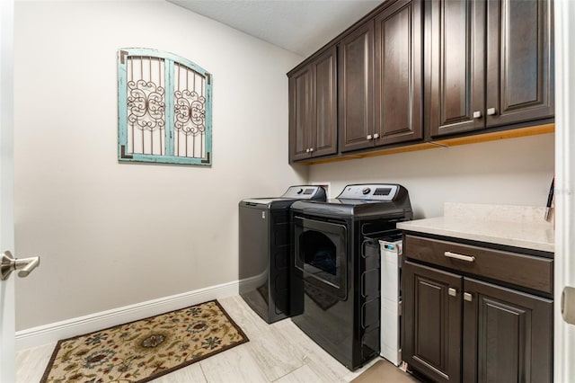 clothes washing area featuring washing machine and dryer, cabinet space, and baseboards