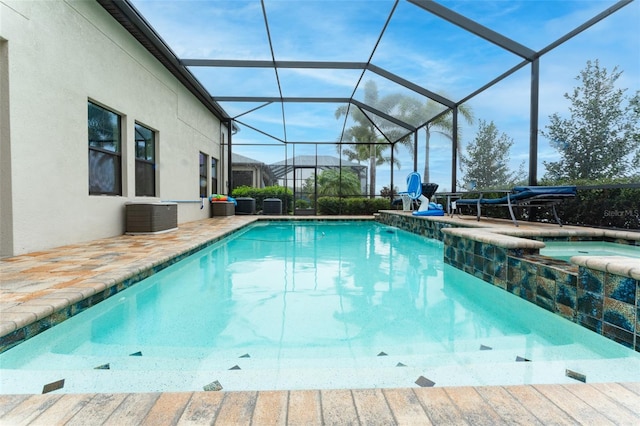 view of pool featuring glass enclosure, a patio area, central AC unit, and a pool with connected hot tub