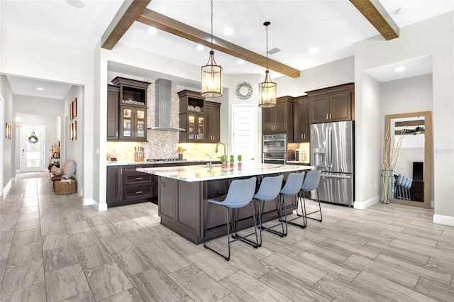 kitchen featuring appliances with stainless steel finishes, beam ceiling, wall chimney exhaust hood, backsplash, and dark brown cabinets