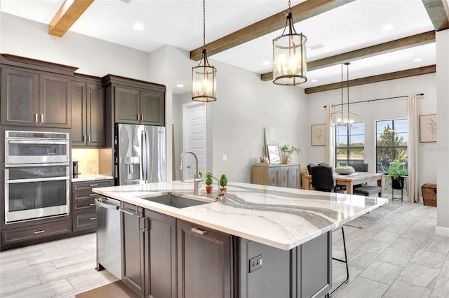 kitchen featuring an inviting chandelier, a sink, beam ceiling, a center island with sink, and appliances with stainless steel finishes
