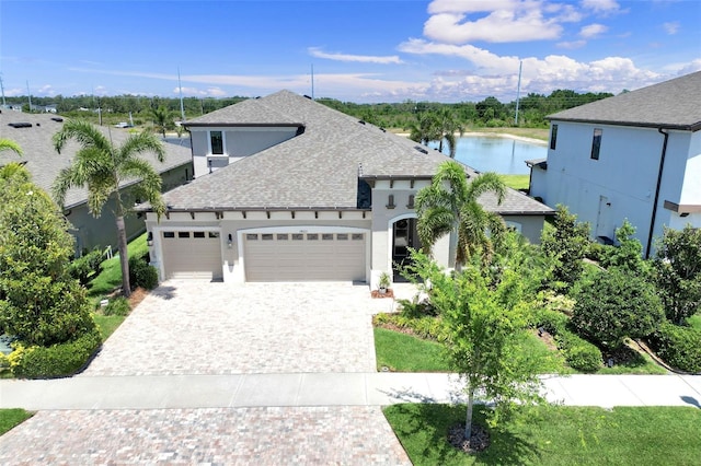 french country home with a shingled roof, stucco siding, decorative driveway, and an attached garage