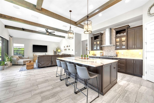 kitchen with stainless steel gas stovetop, decorative backsplash, beam ceiling, a breakfast bar, and wall chimney range hood