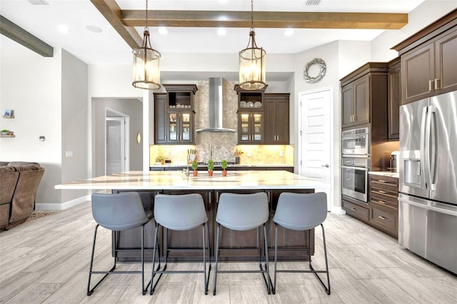 kitchen with decorative backsplash, stainless steel appliances, beamed ceiling, dark brown cabinets, and wall chimney exhaust hood