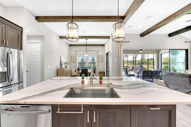 kitchen featuring beam ceiling, stainless steel appliances, a center island with sink, dark brown cabinets, and open floor plan
