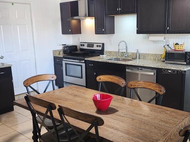 kitchen with light stone countertops, a toaster, light tile patterned floors, stainless steel appliances, and a sink