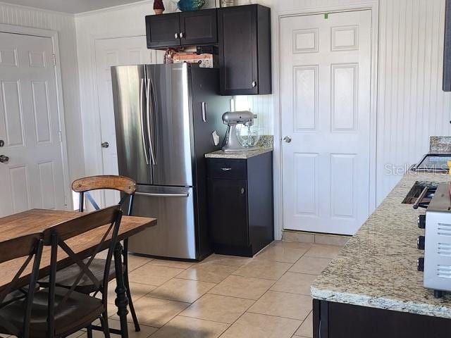 kitchen featuring light tile patterned floors, light stone countertops, dark cabinets, and freestanding refrigerator