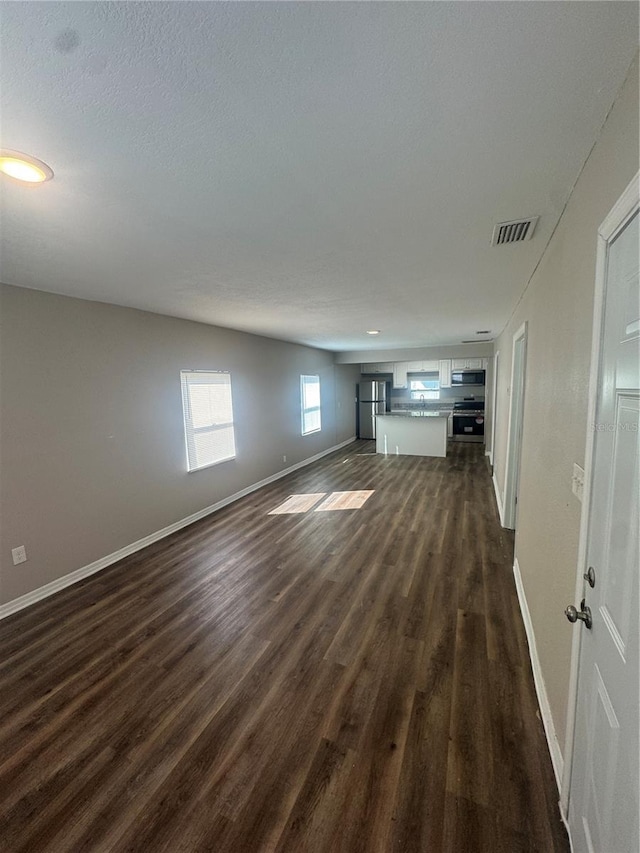 unfurnished living room with baseboards, visible vents, dark wood-style flooring, and a textured ceiling