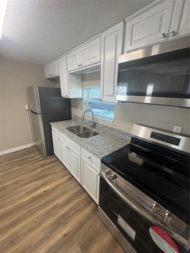 kitchen with dark wood-type flooring, appliances with stainless steel finishes, white cabinets, a textured ceiling, and a sink