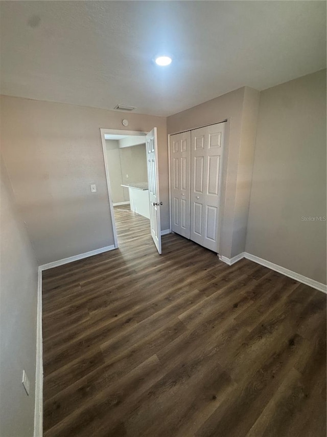 unfurnished bedroom featuring dark wood-type flooring, visible vents, baseboards, and a closet