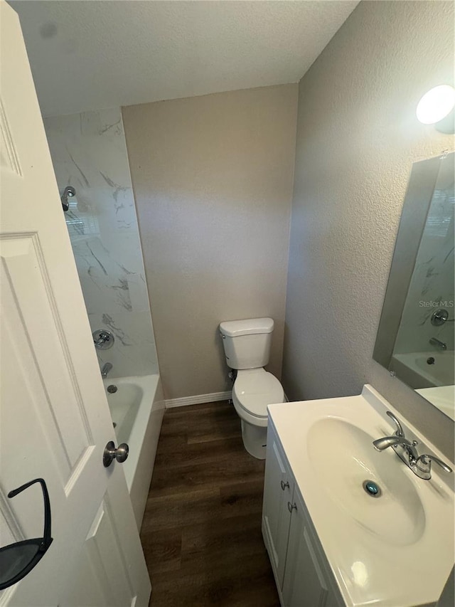 bathroom with toilet, wood finished floors, baseboards, vanity, and a textured wall