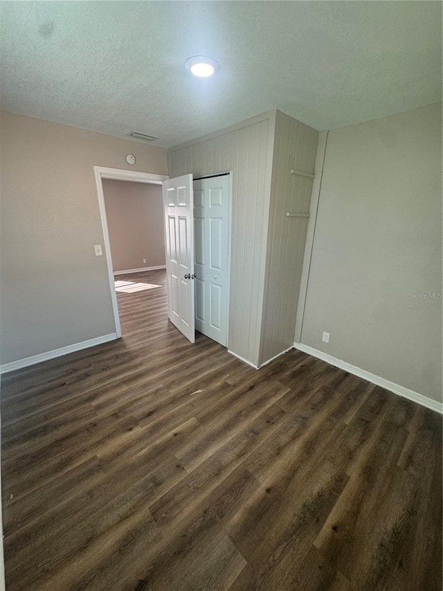 unfurnished bedroom with dark wood-style floors, baseboards, a closet, and a textured ceiling