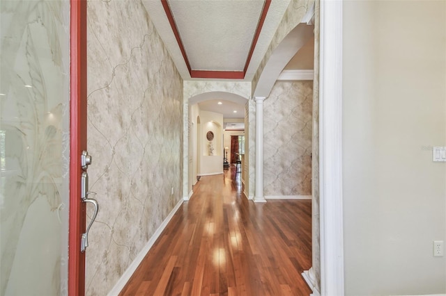 corridor featuring baseboards, arched walkways, wood finished floors, and ornate columns