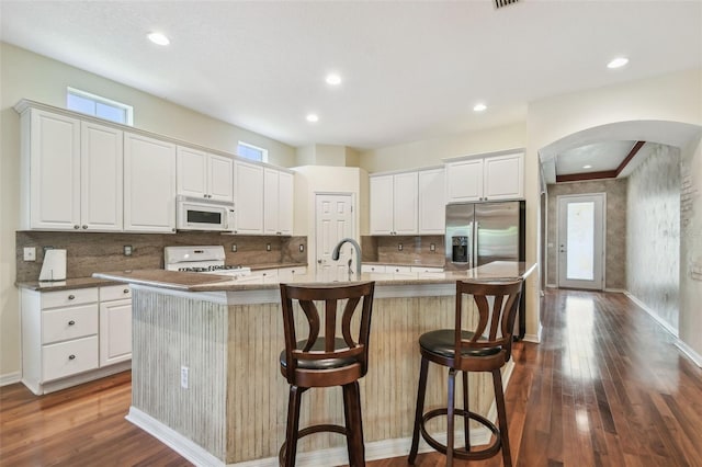 kitchen featuring arched walkways, a healthy amount of sunlight, white appliances, and a large island